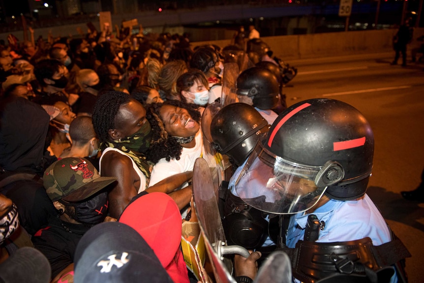 Police with shields hold back a number of protesters