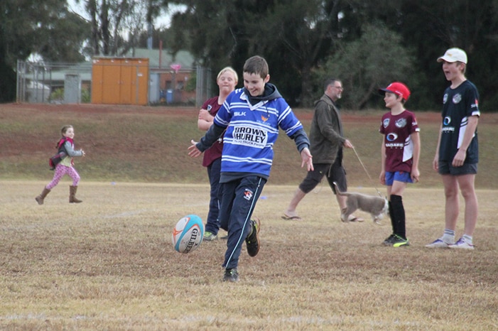 Boy in blue rugby jersey kicks football.