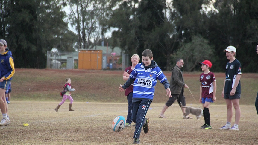 Boy in blue rugby jersey kicks football.