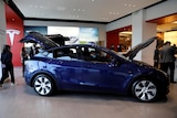 a blue tesla model Y in a showroom with the hood and bonnet up
