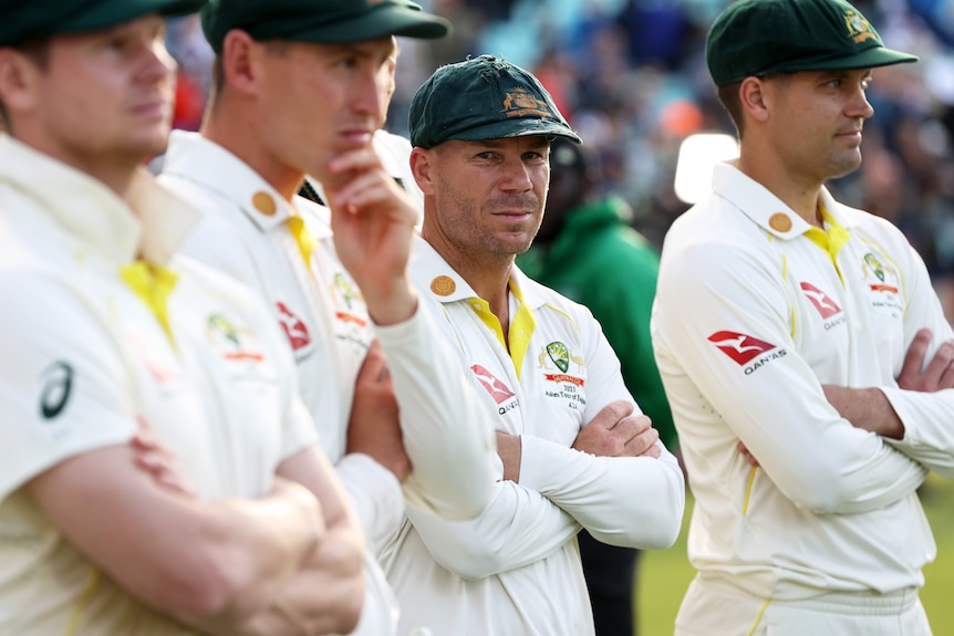 David Warner looks to one side surrounded by his teammates