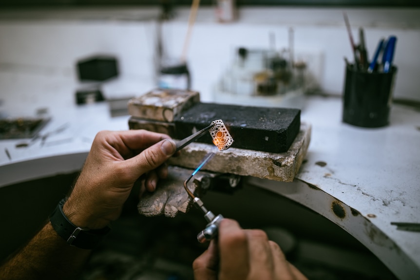 Two hands holding fine tools and working on a piece of jewellery.