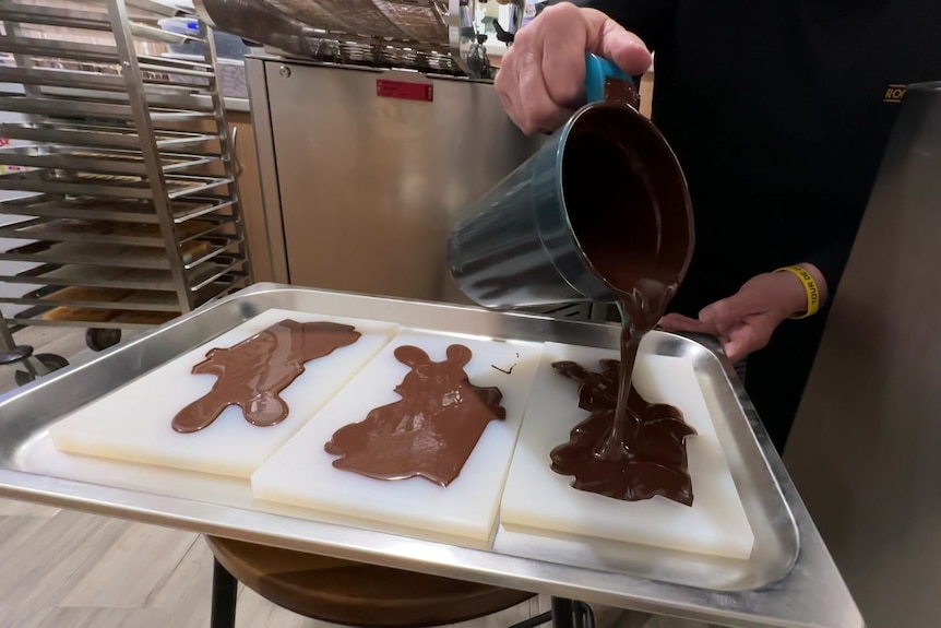 Liquid chocolate poured from a jug into three moulds in the shape of rabbits