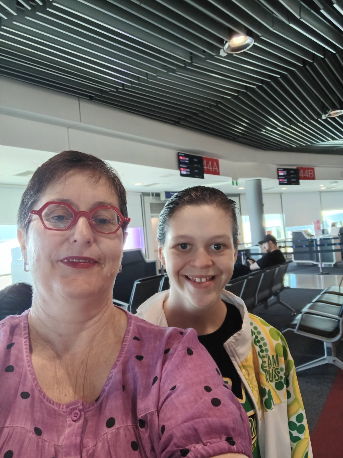 A woman and her teenage daughter talking a selfie at the airport.