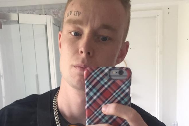 A young man with a tattoo above his right eye takes a photo of himself.