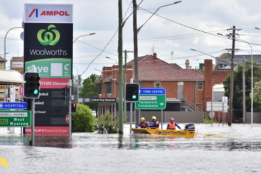 An SES boat driving through a petrol station inundated with water 