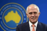 Prime Minister Malcolm Turnbull stands in front of a blue background.