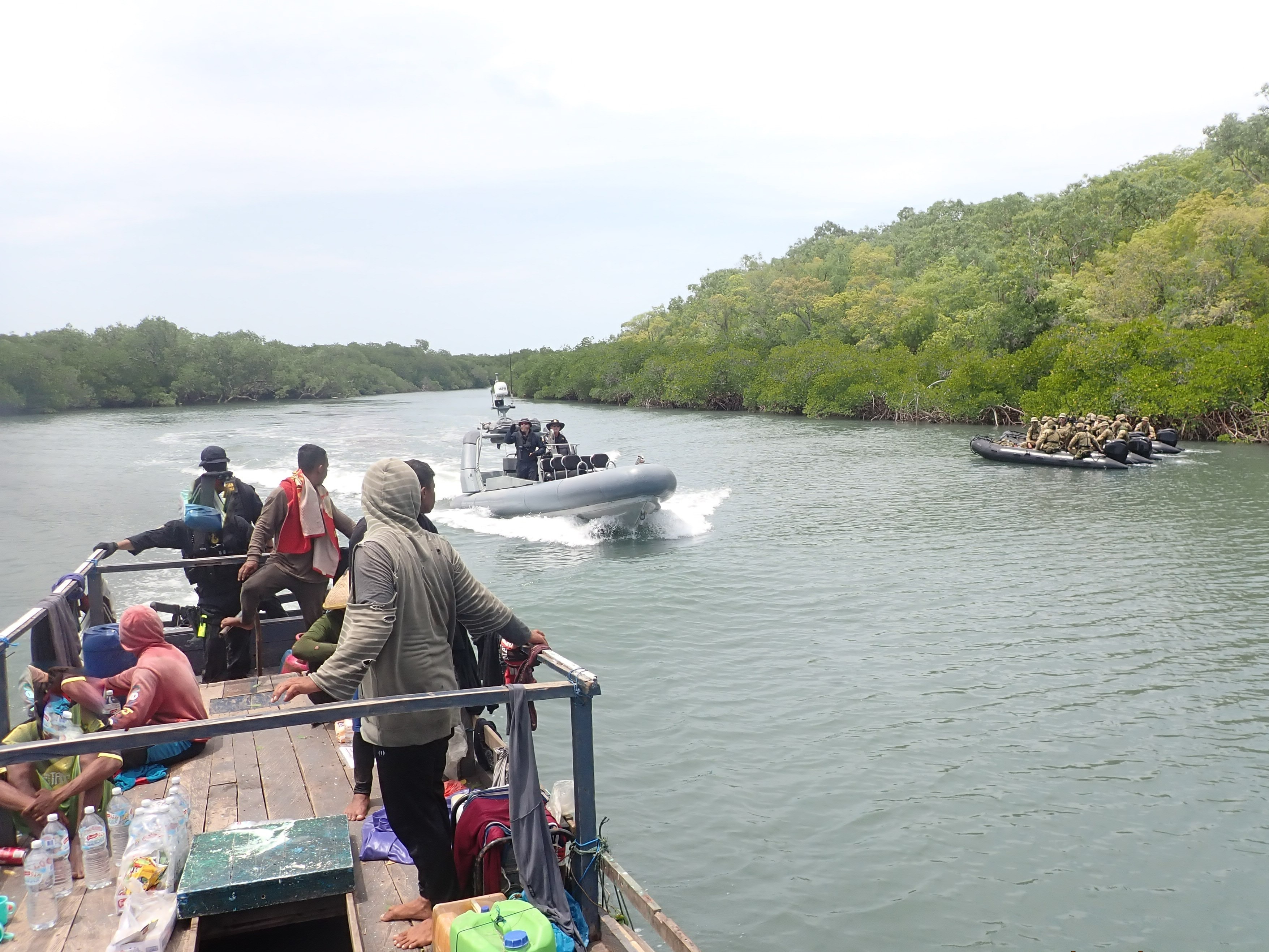 to army boats with troops close in on a small boat with fishers in a mangrove lined river