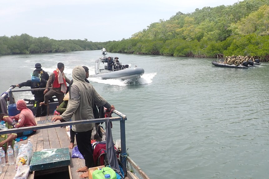 to army boats with troops close in on a small boat with fishers in a mangrove lined river