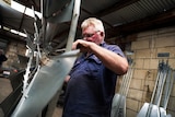 A man in a dirty blue work shirt drills a windmill wheel.