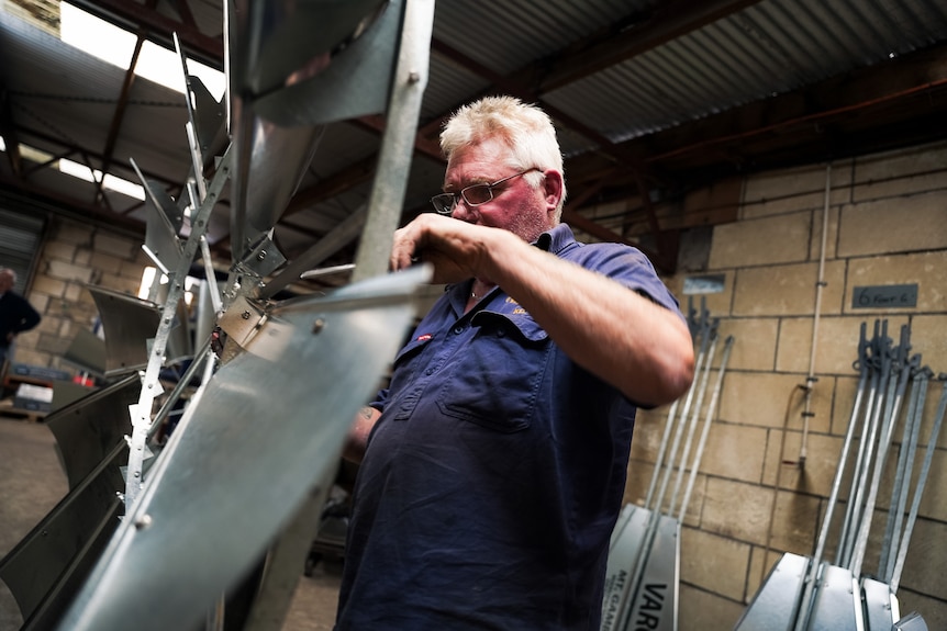 A man in a dirty blue work shirt drills a windmill wheel.