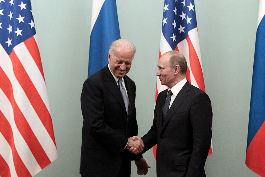 Vladimir Putin and Joe Biden smiling and shaking hands in front of US and Russian flags 