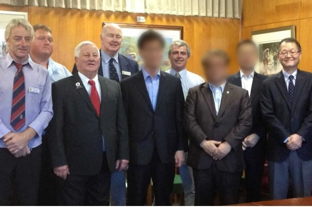 Nine men smile for a photo opportunity in a room.