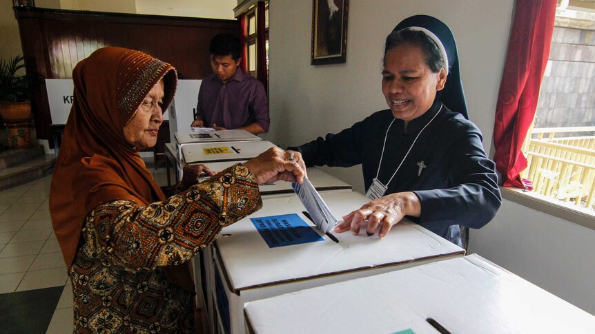 A Catholic nun assists an elderly Muslim woman to cast her ballot.