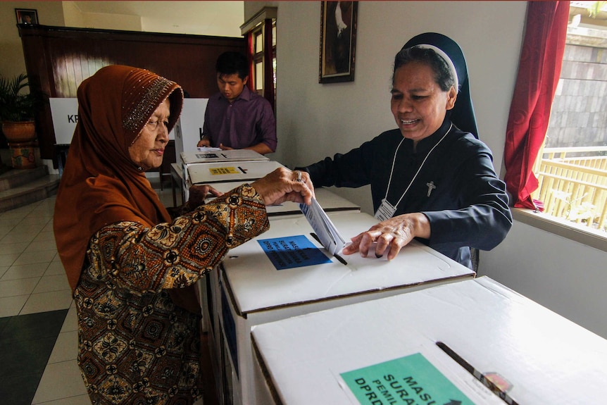 A Catholic nun assists an elderly Muslim woman to cast her ballot.
