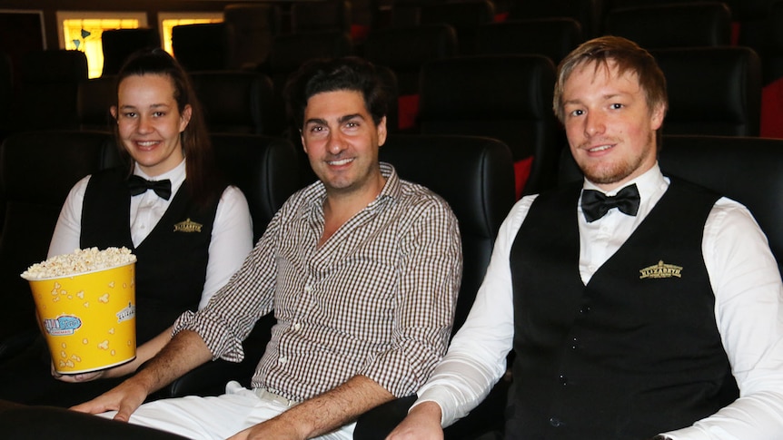 Stephen Sourris (centre) sits with two of his staff in chairs in the Elizabeth Picture Theatre in Brisbane's CBD.
