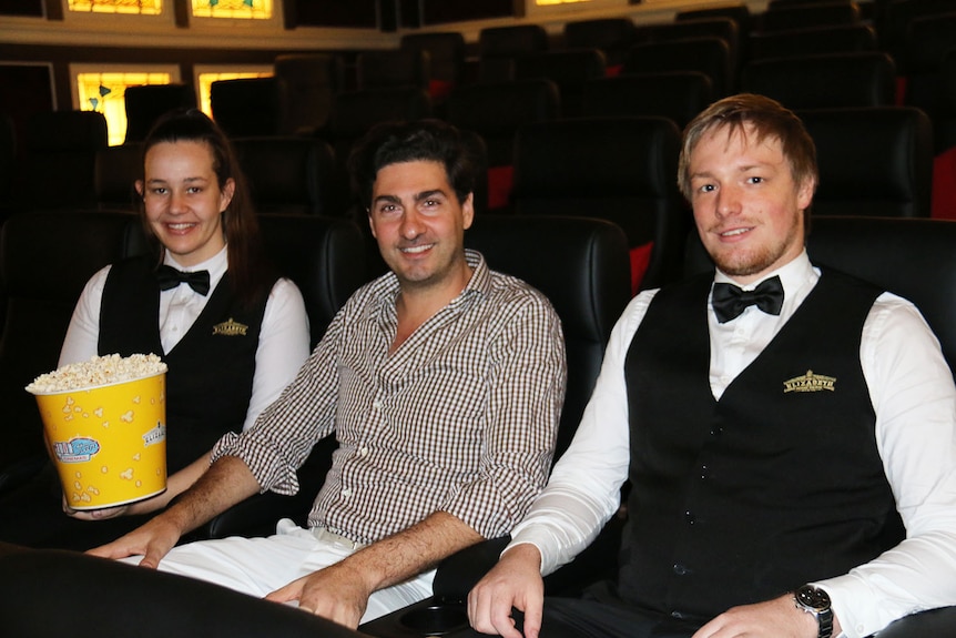 Stephen Sourris (centre) sits with two of his staff in chairs in the Elizabeth Picture Theatre in Brisbane's CBD.