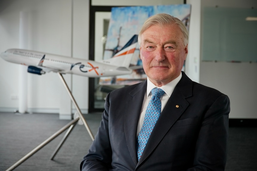 A man wearing a suit and tie sits in front of a model of an aeroplane.