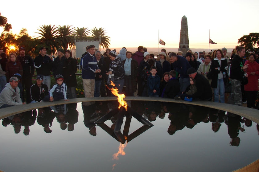A crowd of people gather behind a flame on a pool of water at an Anzac Day dawn service.