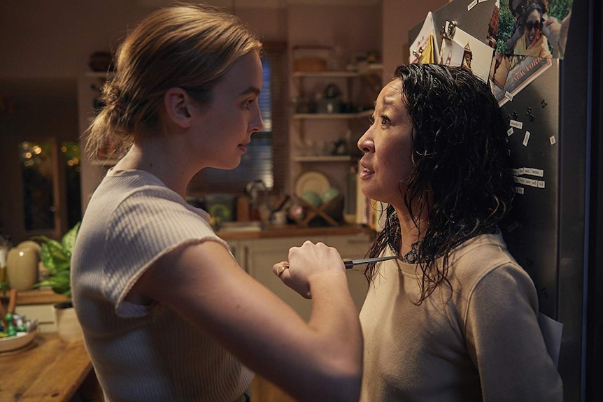 A woman pushes another woman against a fridge and holds a knife to her chest.