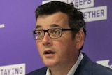 Wearing a suit but no tie, Victorian Premier Daniel Andrews addresses a press conference in front of a purple backdrop.
