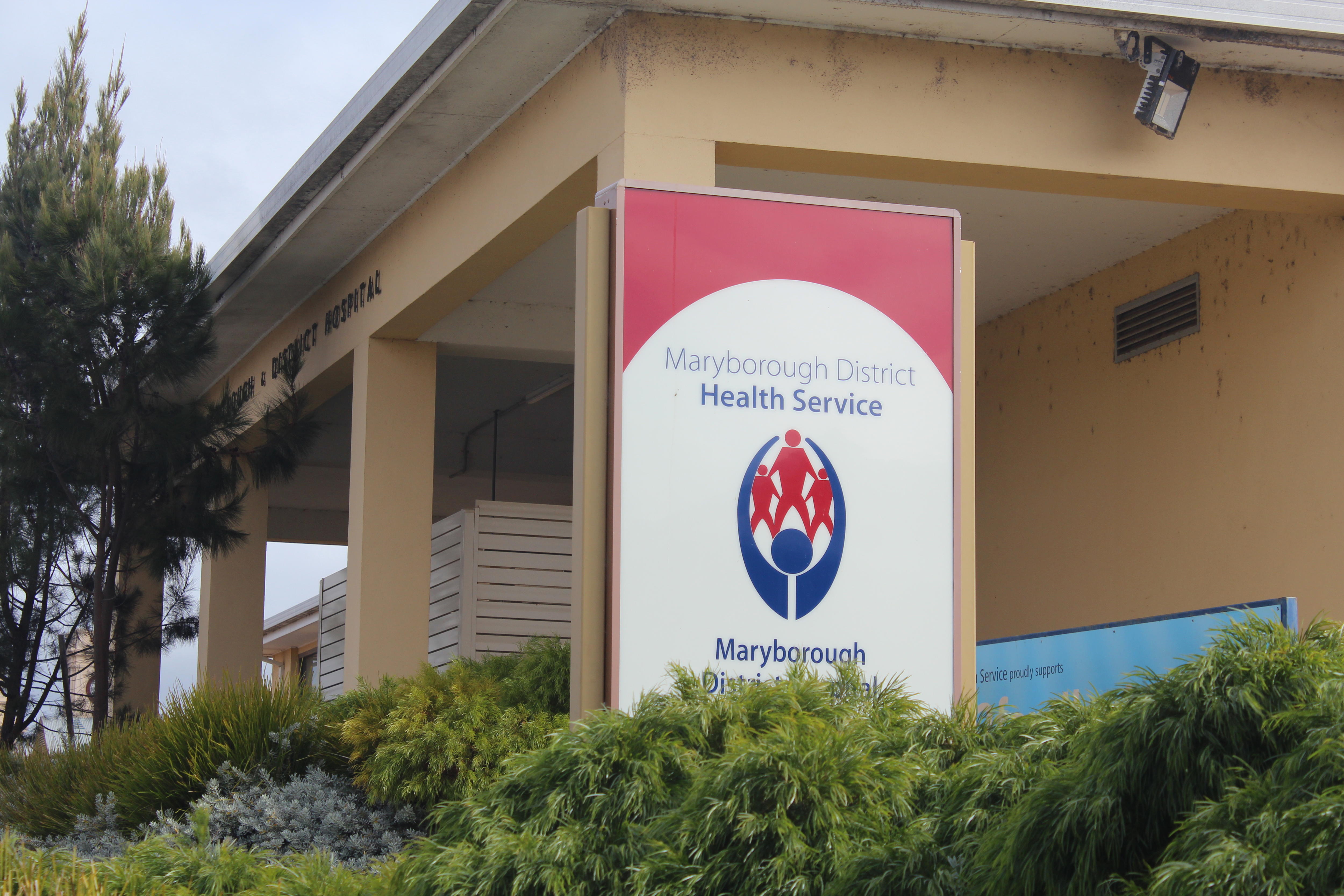 A building with a red and blue sign in front that reads Maryborough District Health Service. 