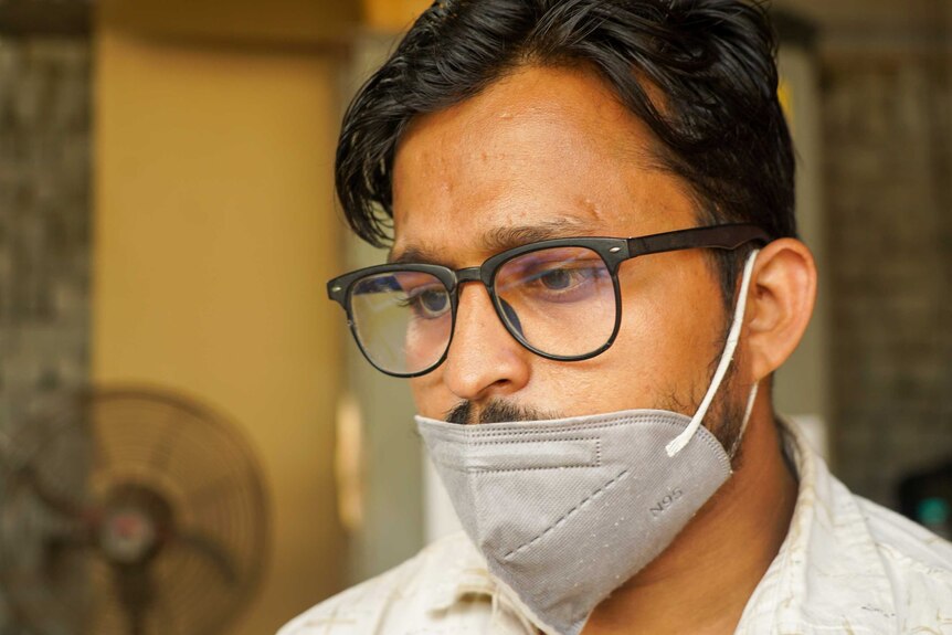 A young man in a glasses with a face mask over his mouth looking sombre