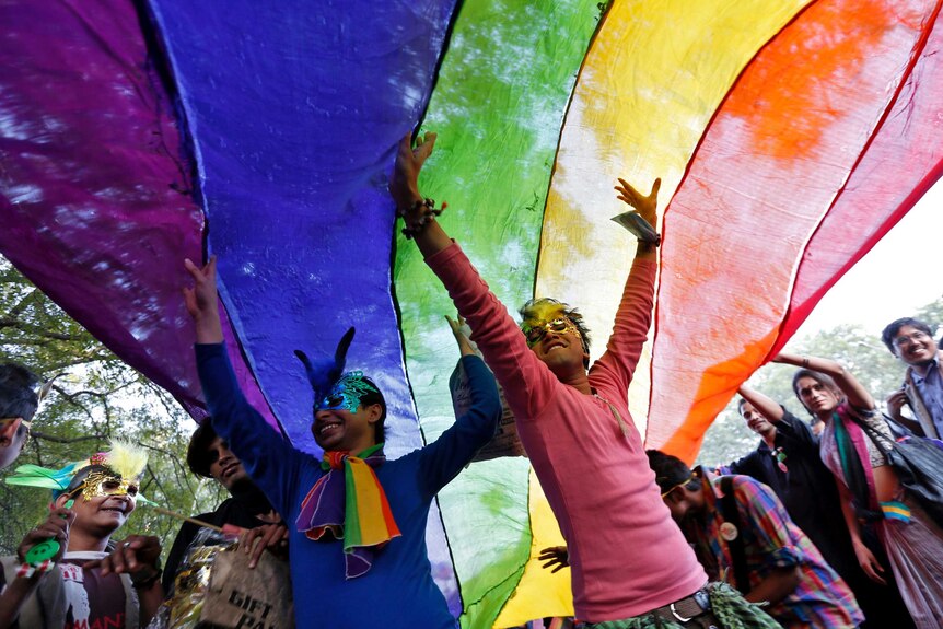 People standing under the rainbow flag wearing face paint. 