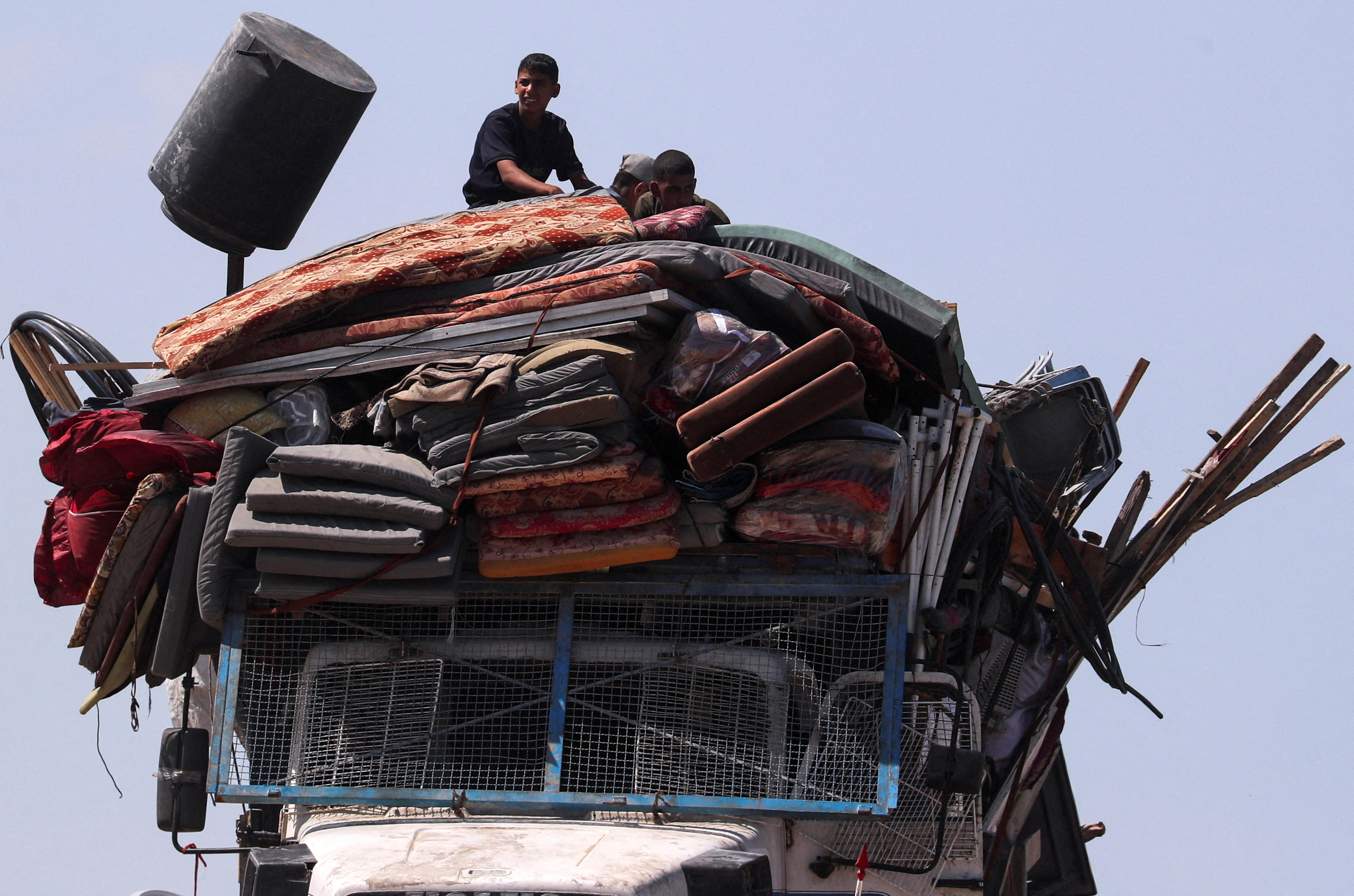 A young boy sitting on top of a truck with dozens of mats, cushions and blankets tied to its roof.