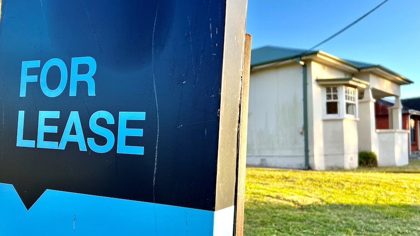 A blue 'for lease' sign outside of a house.