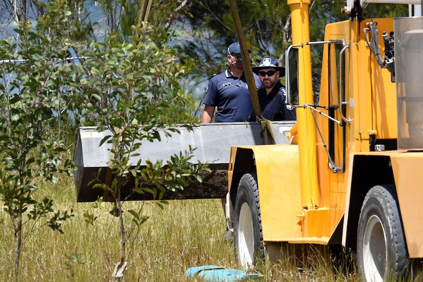 Two policemen watch as a yellow crane truck lifts a black box in grassland