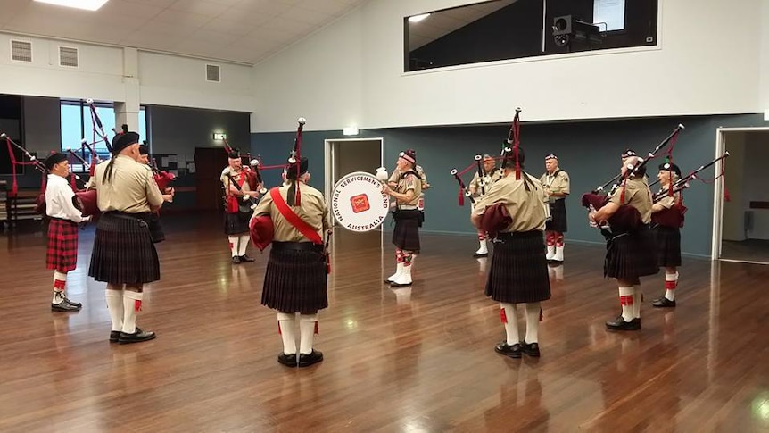 Men wearing kilts and playing bagpipes and drums in a community hall.