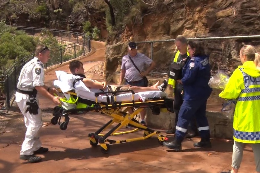 A teenage boy lies on a stretcher while paramedics and police help