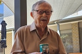 Elderly man smiles as he holds a can of baked beans bearing his likeness.