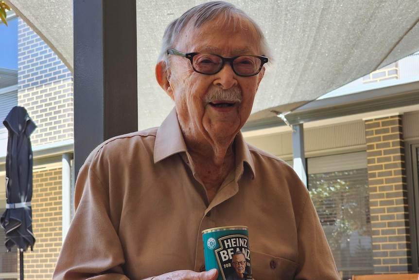 Elderly man smiles as he holds a can of baked beans bearing his likeness.