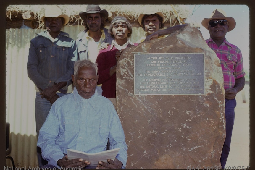 Aboriginal stockmen stand by a plaque attached to a stone.