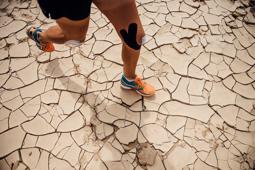 Cracked desert ground with athletic legs wearing orange running shoes, traversing the surface.