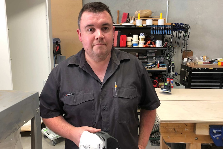 Matthew Canning holding a dust mask in the workshop of is joinery business