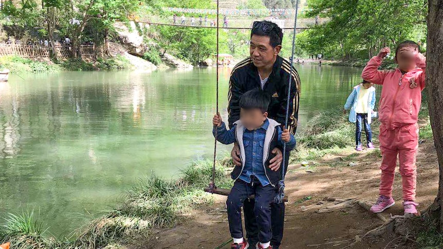 Xiaojun Chen with his children in China, pushes his son on a swing near a river