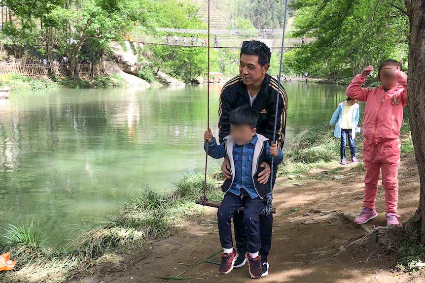 Xiaojun Chen with his children in China pushes his son on a swing near a river