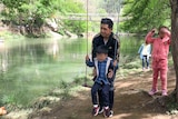 Xiaojun Chen with his children in China, pushes his son on a swing near a river