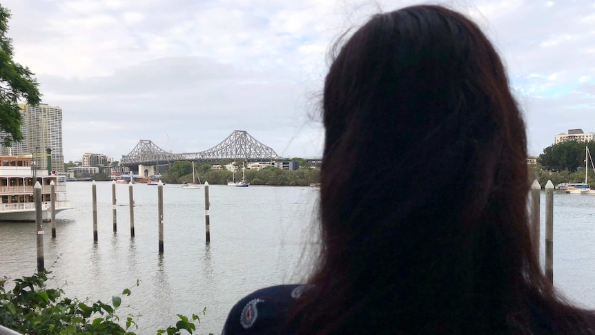 The back of a woman's hair in silhouette as she stands by the Brisbane river.
