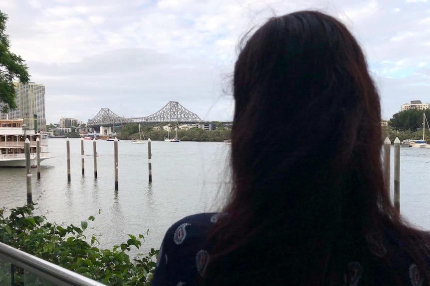 The back of a woman's hair in silhouette as she stands by the Brisbane river.