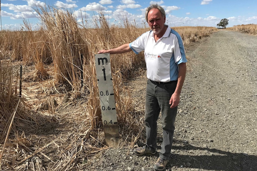 A man standing next to roadside flood marker.