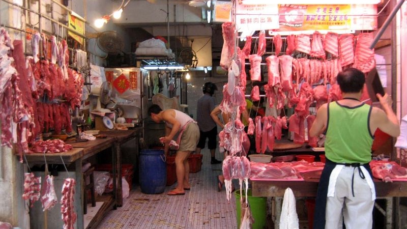 Meat hangs from hooks as two men set up their stalls in a market.