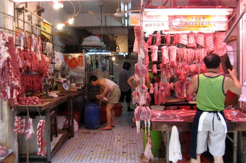 Meat hangs from hooks as two men set up their stalls in a market.