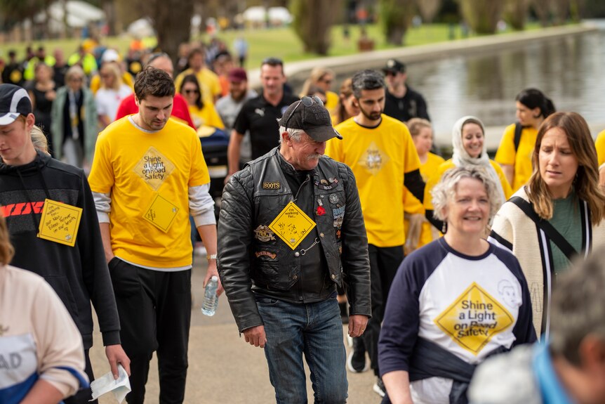 A crowd of people wearing yellow tops walk around a lake to raise awareness about road trauma.