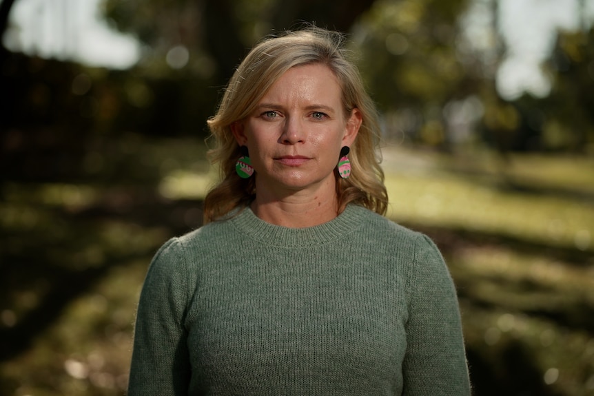 a woman wearing a green knitted jumper and brightly coloured earrings looking directly at the camera