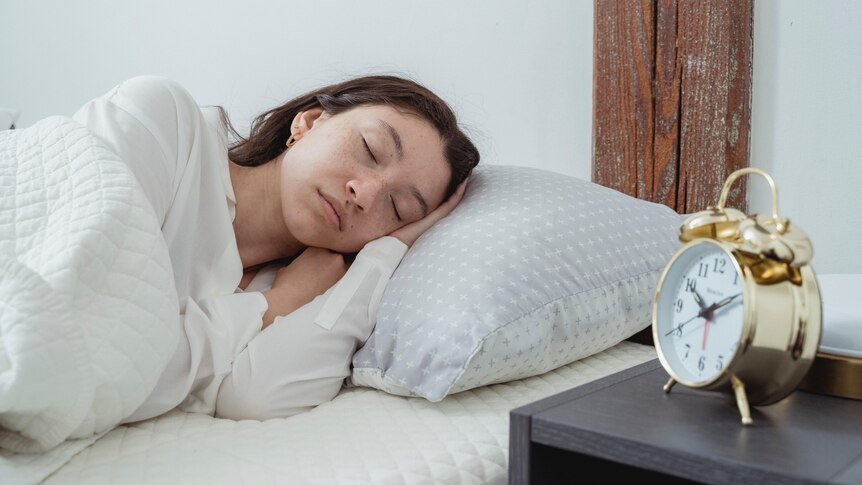 A woman sleeps with an alarm clock on her bedside table.