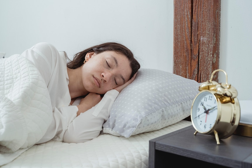 A woman sleeps with an alarm clock on her bedside table.